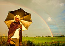 Local man holding an umbrella with double rainbow in the background, Kaziranga National Park, Assam, India. October 2009.