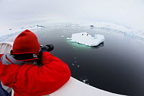 Russell Laman photographing Crabeater seals (Lobodon carcinophaga) on iceberg, The Gullet, Adelaide Island vicinity, Antarctica, February 2011. Model released.