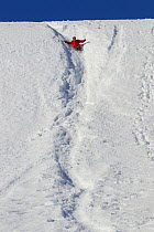 Russell Laman sliding down snowy slope at Neko Harbor, Andvord Bay, Antarctica, February 2011. Model released.