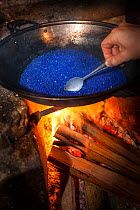 Photographer heating silica gel over camp fire in rainforest to restore its desiccating properties. The high humidity of the rainforest can fog camera lenses and lead to mould growth, so silica gel is used to trap moisture. Maliau Basin, Sabah, Borneo, May 2011.