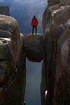 Man standing on Kjeragbolten, a 5 metre boulder stuck in crevice, Kjerag, Lysefjorden, Forsand, Rogaland, Norway, June 2012.