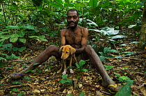 Ba'Kola Pygmy man in forest with dog. Mbomo, Odzala-Kokoua National Park, Republic of Congo (Congo-Brazzaville), Africa, June 2013.