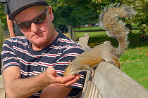 Man feeding Grey squirrel (Sciurus carolinensis) by hand on park bench, St.James's Park, London, UK, September 2014.