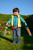 Young boy swinging two garden bird feeders filled with peanuts and fat balls before hanging them up, Bristol, UK, October 2014. Model released.