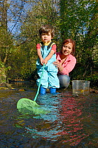 Young boy held by his mother as he dips fishing net into stream, Bristol, UK, October 2014. Model released.