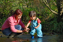 Young boy and his mother peering at stone lifted from stream bed, Bristol, UK, October 2014. Model released.