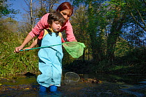 Young boy and his mother fishing net after dipping it into stream, Bristol, UK, October 2014. Model released.