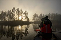 Photographer taking picture of Scots pines (Pinus sylvestris) from canoe on Loch Beinn a' Mheadhoin, Glen Affric, Highlands, Scotland, November 2014.