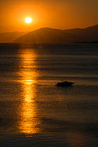 Sunset reflected on the surface of the Aegean Sea on a calm day with a speedboat, Evia Island, Greece. July 2014.
