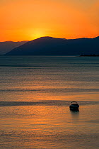 Sunset reflected on the surface of the Aegean Sea on a calm day with a speedboat, Evia Island, Greece. July 2014.