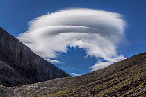 Hikers on trail in the Ubaye valley with Lenticular cloud formation overhead, Alps, France, August 2014.