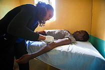 Clinician inserting contraceptive implant into woman's upper arm, at a family health clinic, Kisumu, Kenya.