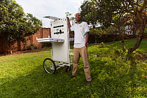 Solar energy entrepreneur poses with his solar kiosk. (Two 40w solar panels charge a lithium ion battery that can charge up to 30 electronic devices at a time) Kigali, Rwanda, June 2014.
