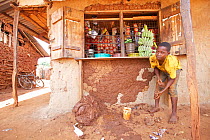 Boy applying clay to traditional style mud wall of shop, Kenya, November 2012.