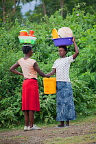 Women talking to each other whilst carrying plastic baskets on their heads, Mfangano Island, Lake Victoria, Kenya, February 2013.