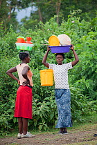 Women talking to each other whilst carrying plastic baskets on their heads, Mfangano Island, Lake Victoria, Kenya, February 2013.
