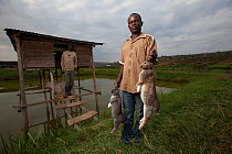Rwandan farmers with rabbits, outside their hutches which sit over a fish-pond, Rwanda, June 2014.