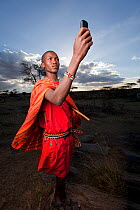 Maasai holding up mobile phone to get better reception, Mara Region, Kenya, September 2013.
