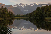 Late evening light on the Southern Alps, reflected in calm waters of Lake Matheson. New Zealand's highest mountain, Mount Cook or Aoraki (3754m) is on the right, and Mount Tasman (3498m) to the left....