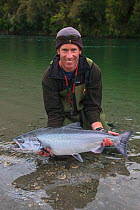Fisherman holding large Chinook / King salmon (Oncorhynchus tshawytscha) West Coast, New Zealand. February 2008. Model Released.
