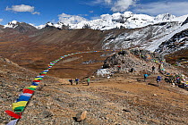Prayer flags and hikers below at 16043 feet (4,380m) Bhonte La pass along the Jhomolhari Trek. Bhutan, October 2014.