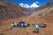 Hikers take a tea break on the asent to Bhonte La Pass (4,380m/16,00ft) the high point of Jhomolhari Trek.  Bhutan, October 2014. Model released.