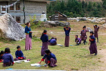 Children in school playground, with teacher standing to the side,  Paro River Valley. Bhutan, October 2014.