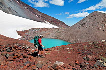 Hiker passing a small lake part way to the summit of South Sister, Three Sisters Wilderness, Deschutes National Forest, Oregon, USA, July 2014. Model released.
