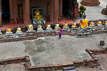 Row of Buddhas with yellow sashes, and woman on phone, Wat Yai Chaya Mongkol, Ayutthaya. Thailand, September 2014.