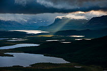 Dark clouds and shaft of sunlight with Stuor Tuvva lake (foreground) and the Patsasj (Petsasj) lake (background), view from Vietovare Mountain. From left to right, mountains Nieras, Alddas and Paljasj...
