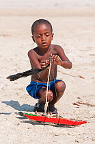 Young Vezo boy, playing with toy boat (pirogue) Morondave, Madagascar. November 2014.