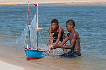 Young Vezo boys, playing with toy boat (pirogue) learning the necessary skills to sail as fisherman, Morondave, Madagascar. November 2014.