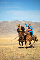 Eagle hunter woman whipping man on slow Mongolian horse to try to slow him down during game at the Eagle hunter's festival. She is on a faster horse but if he wins the game he is entitled to a kiss. E...