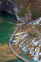 Tourists walking on boardwalk below Velike Kaskade waterfalls, Plitvice Lakes National Park, Croatia. January 2015.