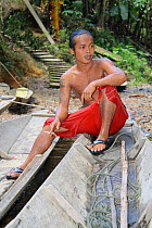 Dayak boy smoking by canoe, West Kalimantan,  Indonesian Borneo. June 2010.