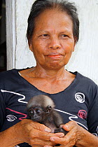 Woman holding orphan baby gibbon (Hylobates) whose mother has been killed in palm oil plantation, Southern Kalimantan, Indonesian Borneo. August 2010.