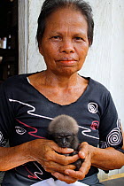 Woman holding orphan baby gibbon (Hylobates) whose mother has been killed in palm oil plantation, Southern Kalimantan, Indonesian Borneo. August 2010.