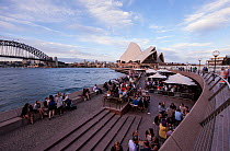 People relaxing in Sydney harbor area, with views of the Harbour Bridge and Opera House, New South Wales, Australia. November 2012.