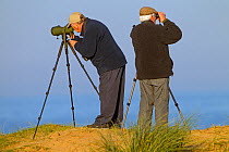 Two male Birdwatchers using a telescope and binoculars  at Titchwell RSPB Reserve, Norfolk, England, UK. November 2014.