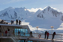 Cruise ship and passengers in front of snow covered mountains, Paradise Bay, Antarctica, January.