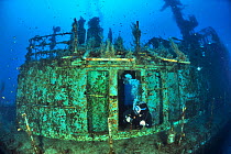 Diver exploring the wreck of the P29 patrol boat scuttled as an artificial dive site in August 2007. Wreck covered in algae and invertebrates and surrounded by fish. Malta, Mediterranean Sea. June 201...