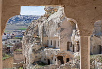View through window carved into rock formation to village with cave houses, near Urgup, Cappadocia, Turkey, March.