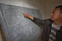 Man pointing at Naxi pictograph character written on blackboard, Yunnan, China