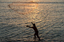 Village chief throwing a cast net catch bait fish by the shore.  Ligau Village, Kia Island, Macuata Province, Fiji, South Pacific. August 2013