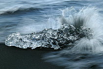 Ice washed up on volcanic sand beach, with waves breaking over it, blurred motion. Near Jokulsarlon, Iceland, August 2003.