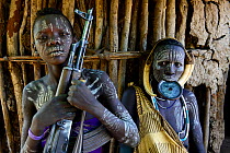 Mursi boy with gun, with mother who has a lip plate, Mursi tribe. Mago National Park. Ethiopia, November 2014