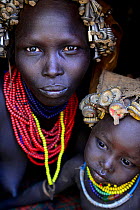 Dassanech woman with headdress of nuts and bolts, her son with headdress of bottle tops. Dassanech tribe, Lower Omo Valley. Ethiopia, November 2014