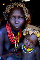 Dassanech woman with headdress of nuts and bolts, her son with headdress of bottle tops. Dassanech tribe, Lower Omo Valley. Ethiopia, November 2014