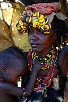 Dassanech woman with child, in traditional clothes, with headdress made from bottlecaps, Lower Omo Valley. Ethiopia, November 2014