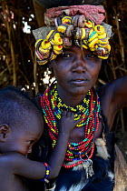 Dassanech woman with child, in traditional clothes, with headdress made from bottlecaps, Lower Omo Valley. Ethiopia, November 2014